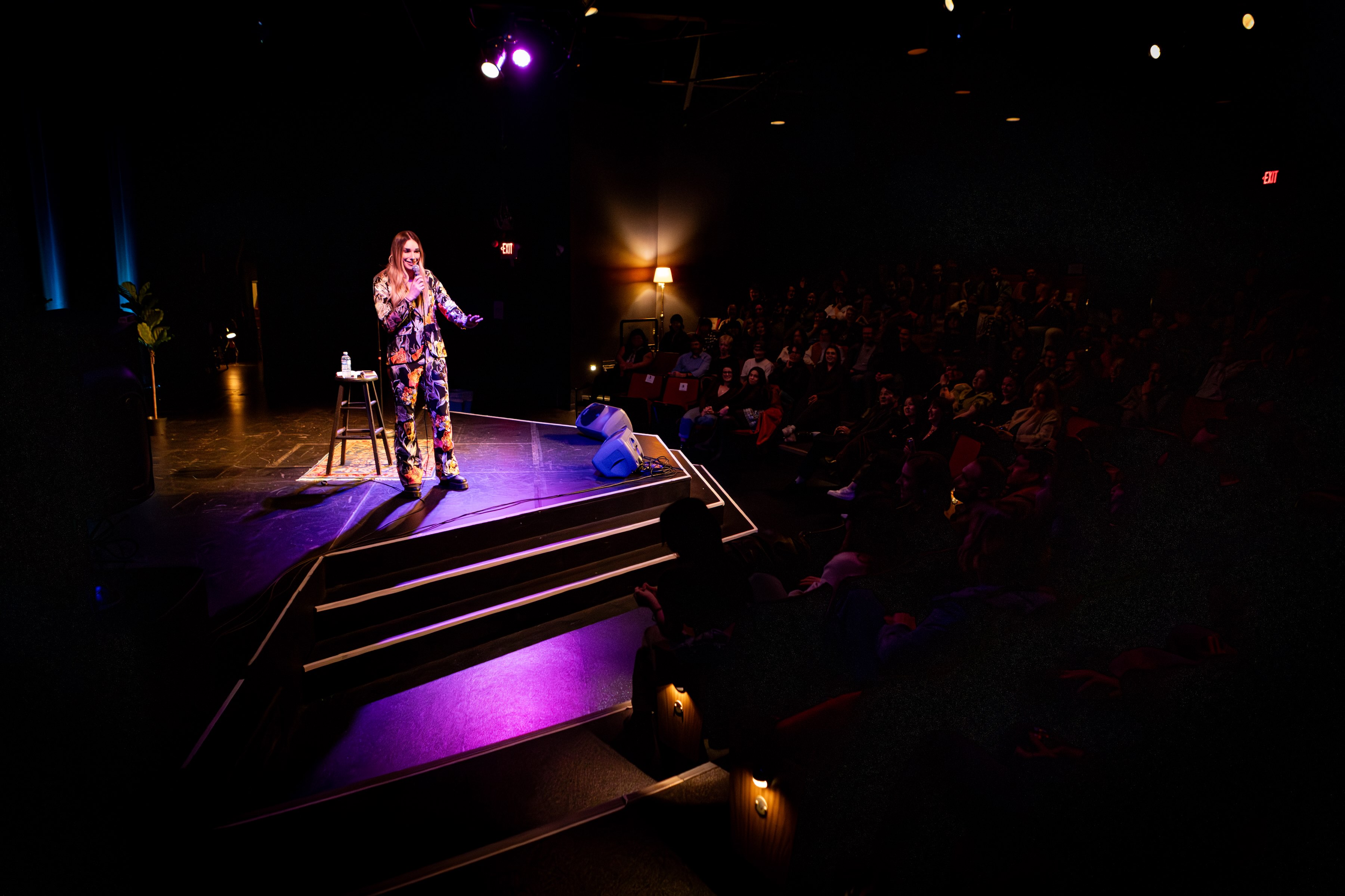 Jess Lupini performing stand-up comedy on stage to a full audience